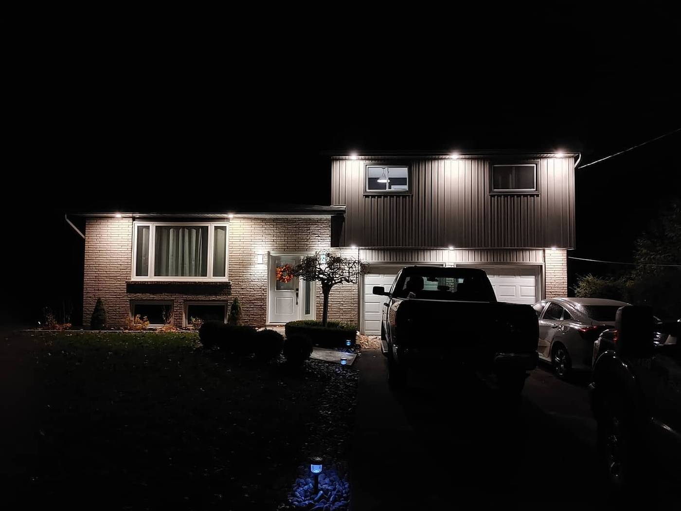 Home exterior at night lit by soffit pot lights and walkway path lighting